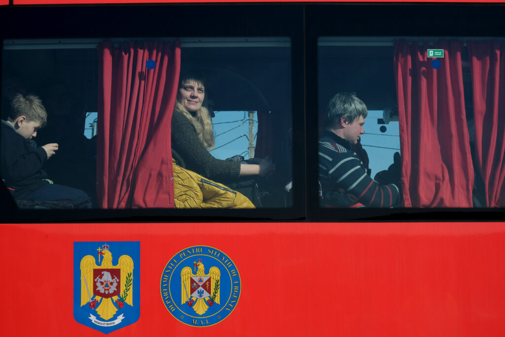 A Ukrainian woman looks out of a bus departing for Bucharest, Romania. From Palanca, refugees were quickly channelled through a cross-border system of redistribution across European countries, based both on individual choice and available capacity in host nations. Palanca, Moldova, 19 March 2022.