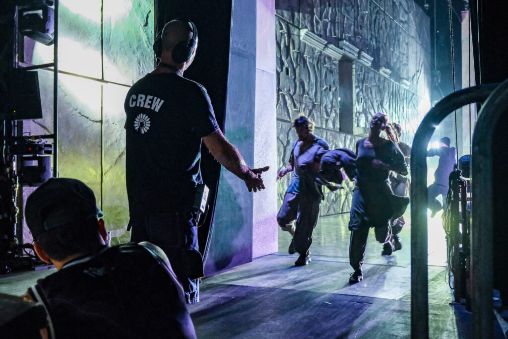 A stagehand waits in the wings for the dancers to run off stage, ready to assist them. In the backstage, performers and technicians move together in a delicate balance of trust and coordination. Milan, September 24th 2022.