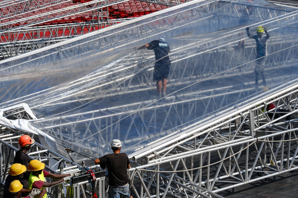 Riggers and stagehands adjust the crystal roof covering of the Space Roof structure during the setup of the stage at the Arena di Verona. July 25th 2022.