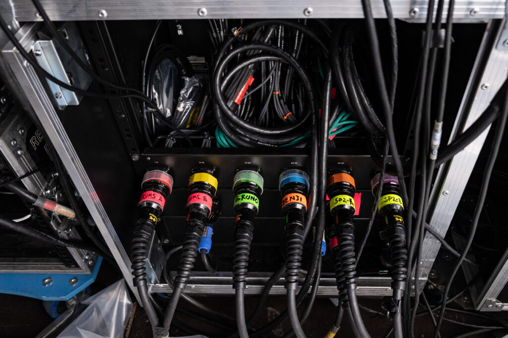 Color-coded audio connections during the setup of a live concert. What appears as a chaotic network of cables is in fact a highly organized system, where every signal has its own precise path and function. Padua, July 2022.