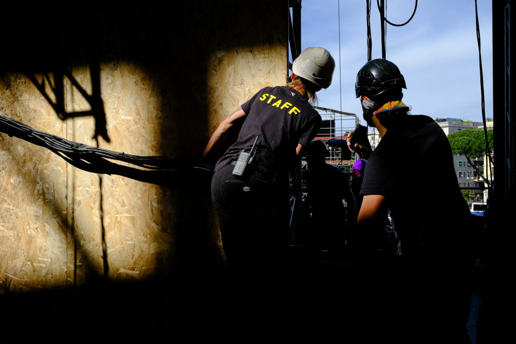 Valentina and Roberto, both riggers, communicate by radio while coordinating the unloading of trucks carrying stage equipment. Rome, April 2023.