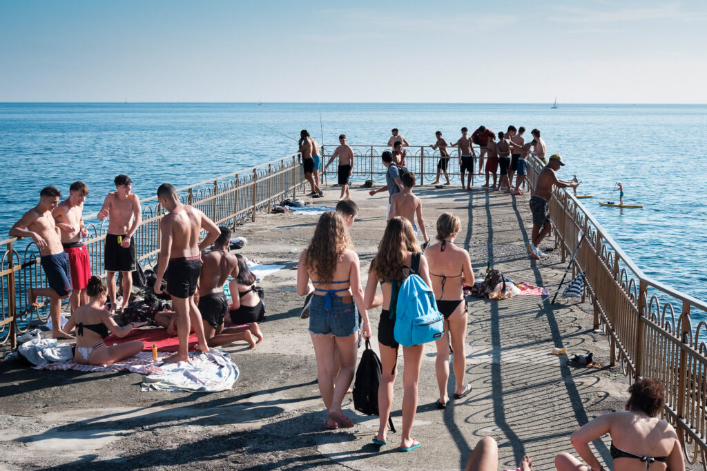 Aware that the cliffs and rocks were not subject to the same controls or restrictions, many people moved into these spaces. The pier becomes a place where young people release months of confinement by diving, pushing each other into the water, helping one another climb back up, and reclaiming physical closeness. Genoa, June 2nd, 2020.